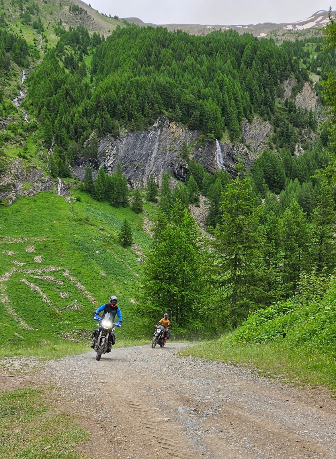 a couple of people riding motorcycles on a dirt road